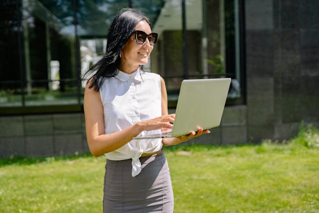 Woman using laptop while standing outdoors.